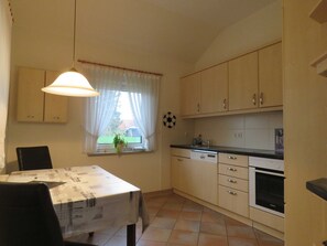 A compact kitchen with a dining table, cabinets, and a window with curtains.