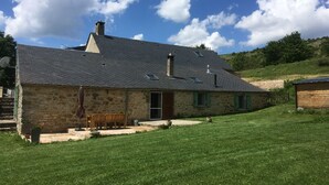 Una casa de piedra con techo inclinado, una chimenea y un pequeño porche con un banco.
