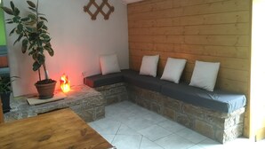 Un rincón acogedor con un banco de piedra y cojines, una planta en maceta y una pequeña chimenea.