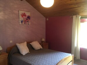 A bedroom with a bed, two bedside tables, a nightstand, a wall painting, and a window with curtains. - Cottage on the Causse Mejean (Montbrun)