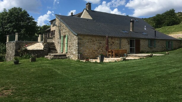 Una casa de piedra con techo inclinado, un pequeño porche y un patio cubierto de césped.