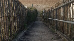 A wooden staircase leading to a sandy beach with a fence on either side.