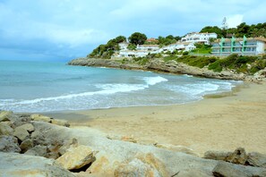 A coastal beach with rocky foreground, calm sea, and hillside buildings. - OFFER PENTHOUSE GRAND Solarium PRIVATE, CONDITIONED, POOL, VERY QUIET, WIFI (Salou)