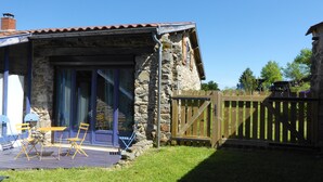 Een gebouw van steen met een pannendak, een houten terras met stoelen en een houten poort.