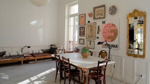 A dining area with a white table, wooden chairs, and a large vase. There is a bench with cushions and a wall with framed pictures and a mirror. - La Terrasse du Soleil:Fantastic 3-bd apt with sundeck facing the beach! (Menton)
