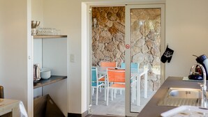 A modern kitchen with a gas stove, a sink, and a stone wall. There is a dining area visible through an open door.