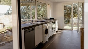 A modern kitchen with a dishwasher, washing machine, and a large window overlooking a garden.