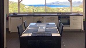 A modern kitchen with a large island, a dining area with a table and chairs, and a view of a mountainous landscape through large windows.