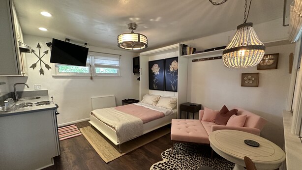 Une chambre compacte comprenant un lit, un canapé, une petite table, un téléviseur et un coin cuisine.