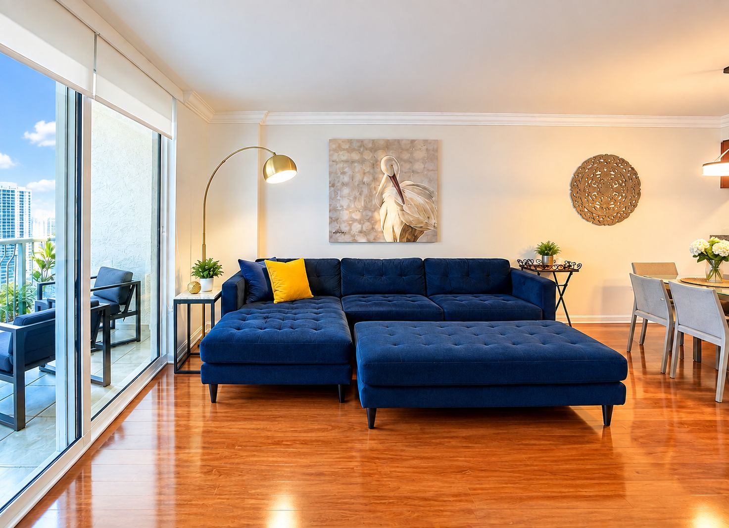 A modern living room with a sectional sofa, a dining table, and a large window offering a city view.