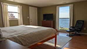 Ein Schlafzimmer mit Bett, Fernseher, Stuhl und Blick auf das Wasser.