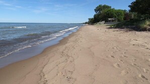 Ein sandiger Strand mit blauem Himmel, einigen Bäumen und einem kleinen Gebäude rechts.