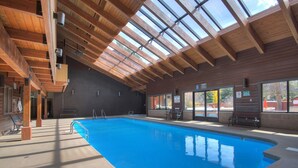 En indendørs swimmingpool med træloft og store vinduer.