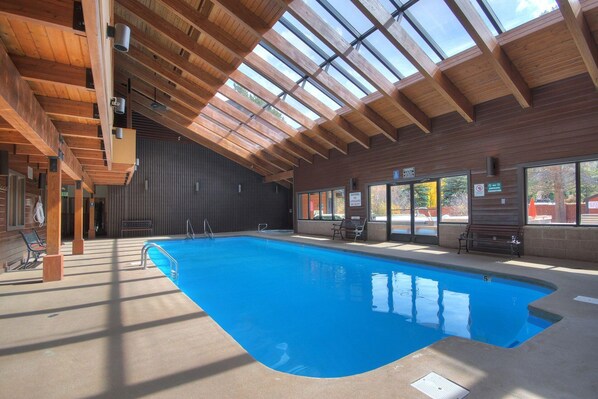 An indoor swimming pool with a wooden ceiling and large windows.