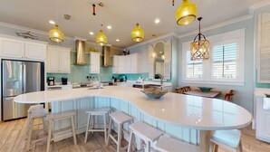 Una cucina moderna con un'isola grande, mobili bianchi e illuminazione a sospensione.