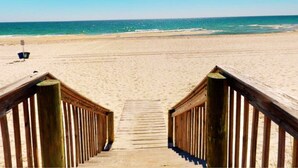Una passerella in legno conduce a una spiaggia sabbiosa sotto un cielo azzurro limpido.