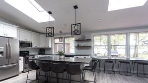 Una cocina moderna con una isla grande, taburetes de bar, electrodomésticos de acero inoxidable y vistas al exterior.