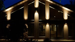 Un edificio moderno con fachada de madera y grandes ventanales, iluminado por luces exteriores.