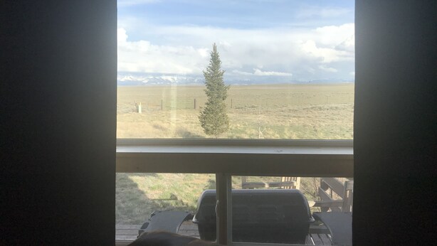 Une vue à travers la fenêtre d’une pièce donnant sur un champ verdoyant et des montagnes au loin.