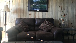Un salon avec un canapé en cuir marron, un téléviseur fixé au mur et un mur en bois.