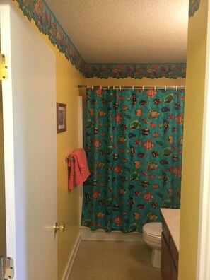 Une salle de bain avec un rideau de douche orné de motifs colorés représentant des poissons, des toilettes et une serviette accrochée au mur.