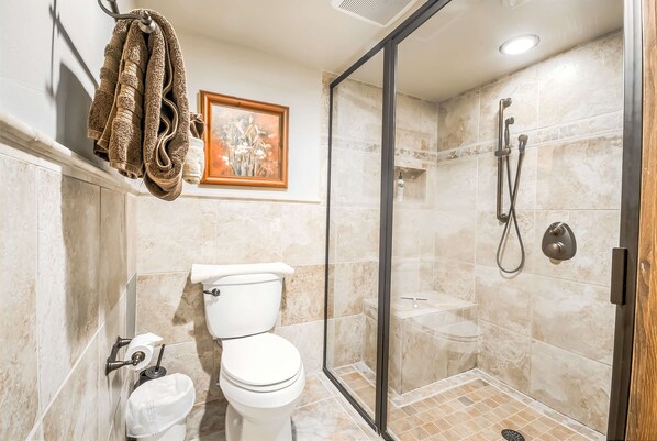 Une salle de bain comprenant des toilettes, une douche et un espace de douche fermé par des parois en verre.