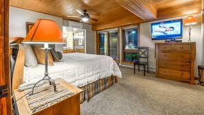 A bedroom with a bed, a desk, a lamp, a dresser, a television, and a ceiling fan.