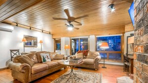 A cozy living room with a wooden ceiling, two leather sofas, a coffee table, and a large window.
