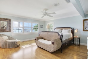 A bedroom with a bed, a chair, a ceiling fan, and a window.