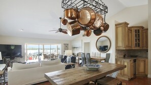 Un salón espacioso con un sofá blanco, una mesa de comedor de madera y una zona de cocina con armarios de madera y ollas de cobre colgando del techo.