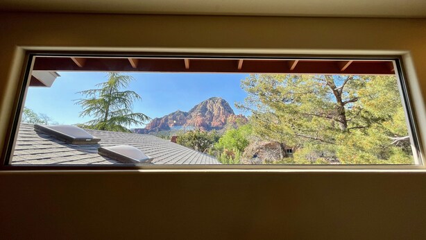 Une fenêtre donnant sur une montagne, des arbres et un bâtiment.