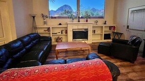 Un salon doté d’une cheminée, d’un canapé en cuir noir, d’une table basse en bois et d’une grande fenêtre offrant une vue sur les montagnes.