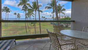 A balcony with a view of palm trees and the ocean. There is a round table and two chairs. - Leinaala Oceanfront 405 Panoramic Ocean View, Great Rates, Steps to the beach (Kihei)