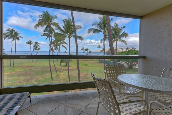 A balcony with a view of palm trees and the ocean. There is a round table and two chairs.