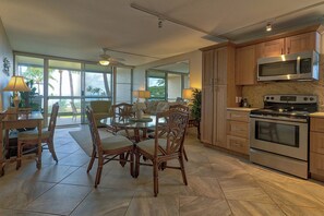 A spacious kitchen with wooden cabinets, a microwave, and an oven. There is a dining area with wicker chairs and a table. - Leinaala Oceanfront 405 Panoramic Ocean View, Great Rates, Steps to the beach (Kihei)