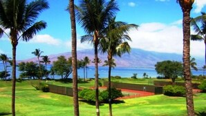 A view of a golf course with palm trees and a body of water in the background. - Leinaala Oceanfront 405 Panoramic Ocean View, Great Rates, Steps to the beach (Kihei)