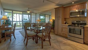 A spacious kitchen with wooden cabinets, a microwave, and an oven. There is a dining area with wicker chairs and a table. - Leinaala Oceanfront 405 Panoramic Ocean View, Great Rates, Steps to the beach (Kihei)