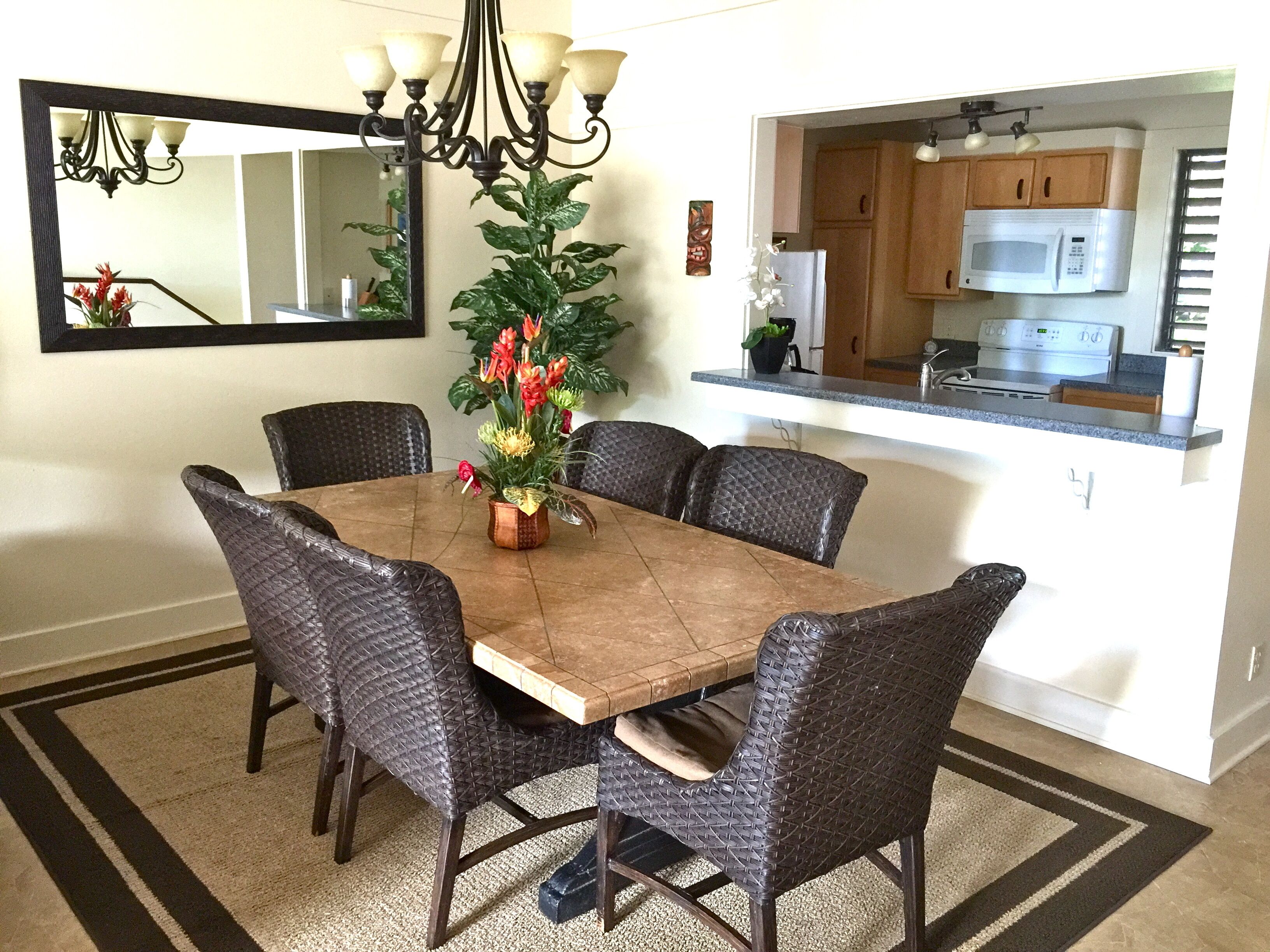 A dining room with a wooden table surrounded by six chairs, a chandelier, and a potted plant with flowers.
