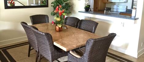 A dining room with a wooden table surrounded by six chairs, a chandelier, and a potted plant with flowers.