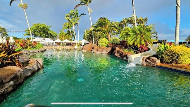 A clear pool with a water slide, surrounded by palm trees and tropical plants. - 2/2 BEACH FRONT RESORT-AC-Poipu Bch, Kiahuna-Garden View, Pool/Gym/Courts (Poipu Beach)