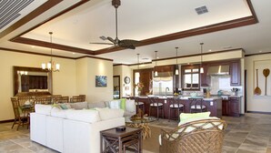 A spacious living room with a large sofa, dining area, kitchen, and a ceiling fan. - BIG ISLAND PARADISE-private lanai -pool/spa/low golf rates/access to #1 beaches  (Kamuela)