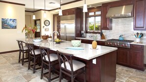A spacious kitchen with a large island, dark wooden cabinets, stainless steel appliances, and a view of the outdoors. - BIG ISLAND PARADISE-private lanai -pool/spa/low golf rates/access to #1 beaches  (Kamuela)