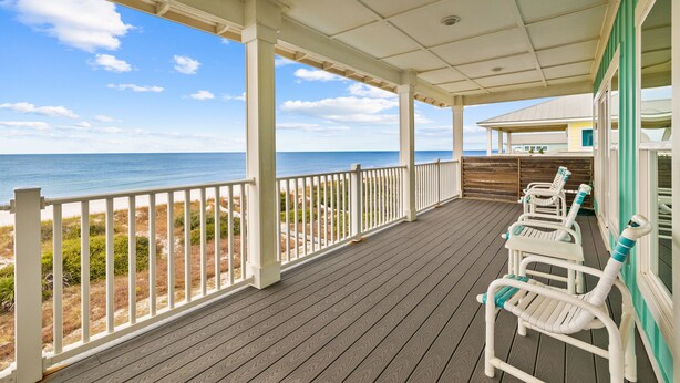 A covered deck with a view of the ocean, wooden chairs, and a building in the background. - Cape Conchs: Large Beachfront Home, Private Pool, Sleeps 18, Pet Friendly (Cape San Blas)