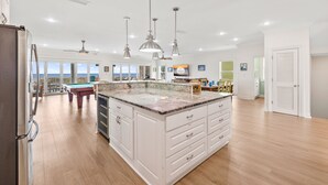 A spacious kitchen with a central island, pendant lighting, and a view to the outside. - Cape Conchs: Large Beachfront Home, Private Pool, Sleeps 18, Pet Friendly (Cape San Blas)