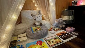 Um recanto acolhedor para leitura, com um banco estofado, um brinquedo macio e diversos livros.