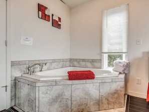 Un baño con lavamanos de mármol, una alfombra de baño roja y una ventana con persianas.