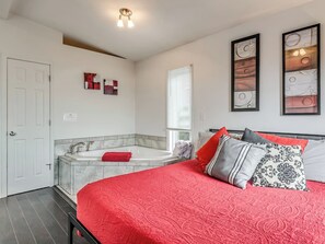 A bedroom with a large bed, a built-in bathtub, and a window with blinds.