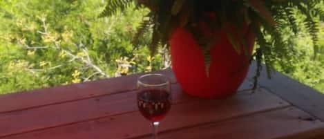 Une table en bois, sur laquelle se trouvent un pot de fleurs et un verre de vin rouge.