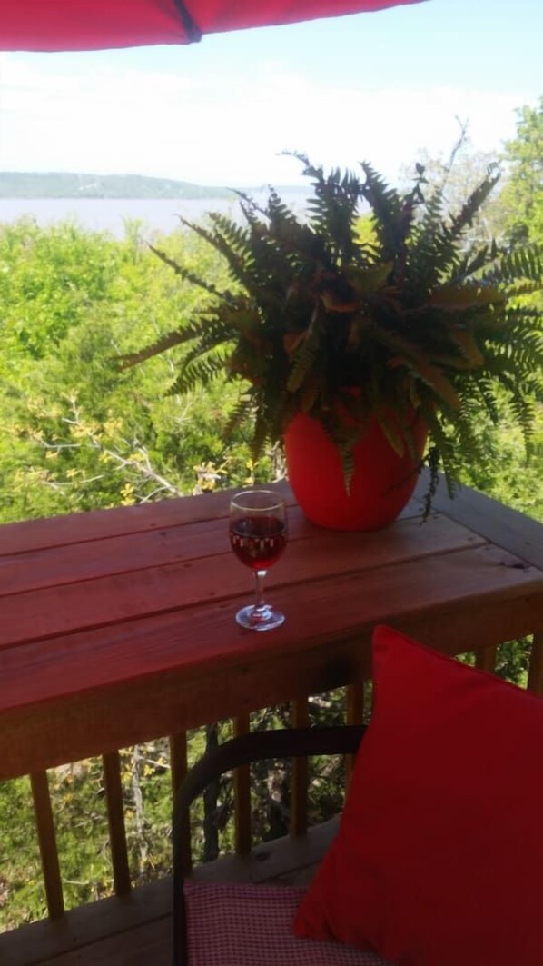 Une table en bois, sur laquelle se trouvent un pot de fleurs et un verre de vin rouge.