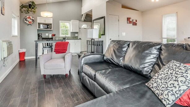 A modern living room with a leather sofa, a white armchair, and a dining area with a kitchen in the background. - Romantic Lakeview Treehouse with Private Jacuzzi (Stigler)